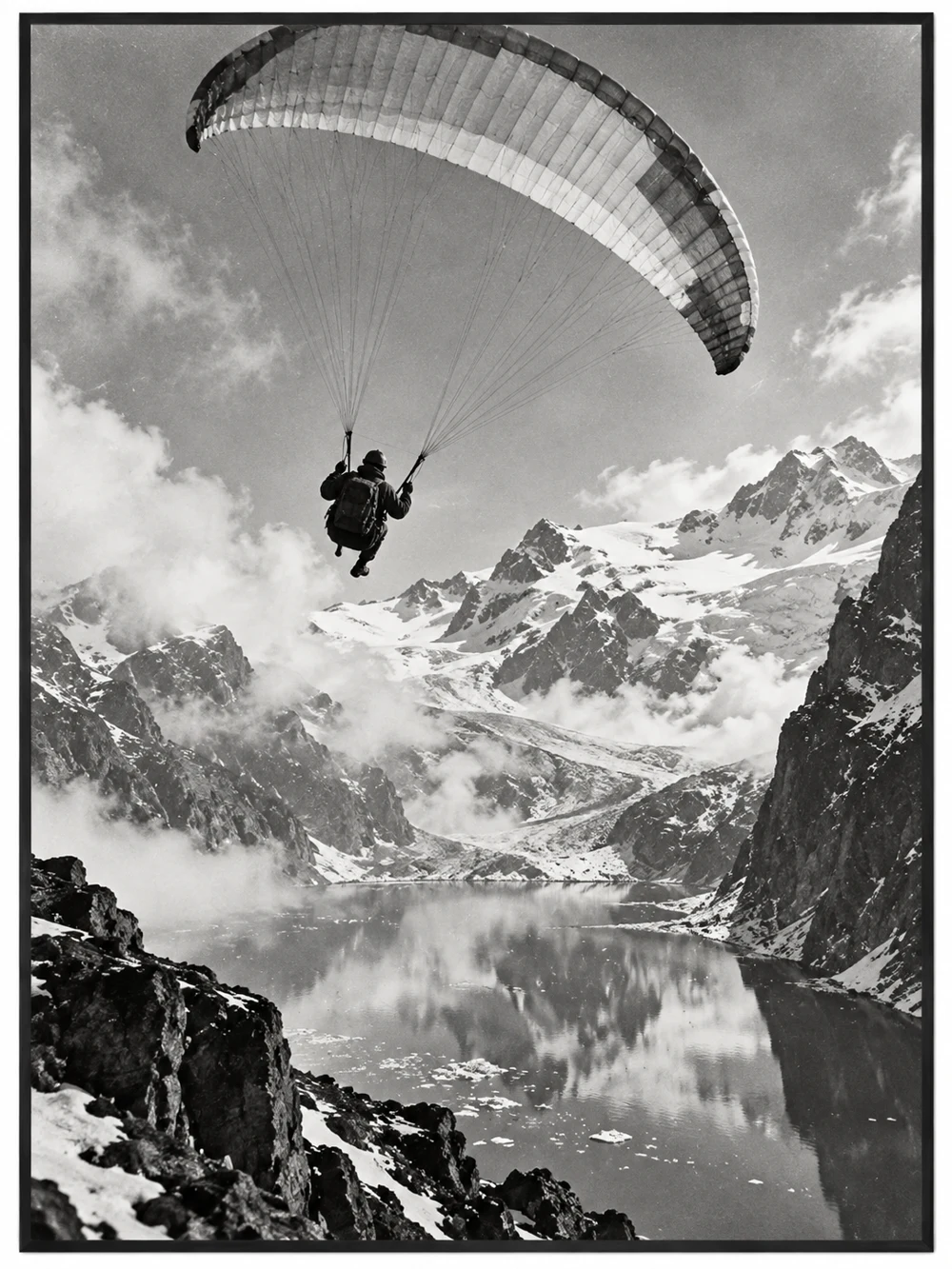 Schwarz-weisses Bergmotiv mit einem Gleitschirmflieger über einem Alpensee